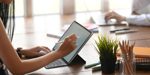 Cropped image of graphic designer writing/sketching on white blank screen computer tablet by using...