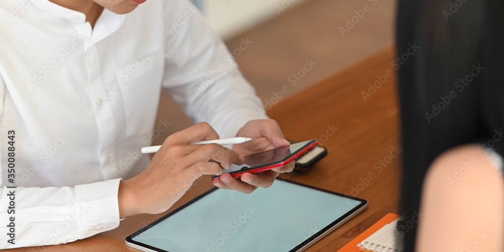 Poster cropped image of business man holding a stylus pen and smartphone while sitting in front of white bl