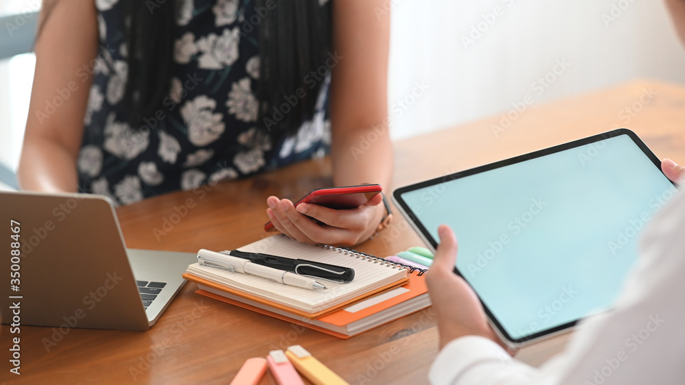Poster cropped image of businessman holding a white blank screen computer tablet while sitting in front of 