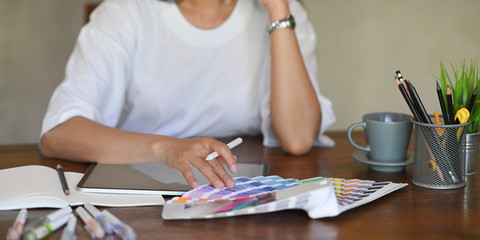 Photo of young graphic designer holding a stylus pen while selecting color from color guide and...