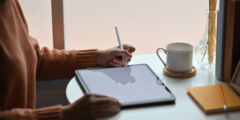 Closeup woman drawing/sketching on computer tablet by using a stylus pen while sitting at the...