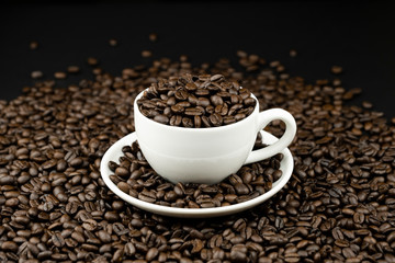 Roasted coffee beans in a white coffee cup on coffee beans field background