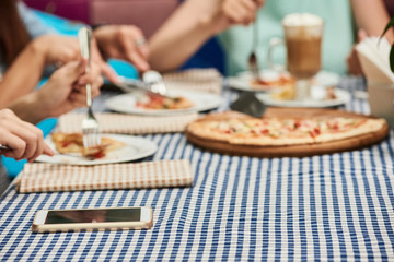 Smartphone lying on table while women eating pizza, closeup photo