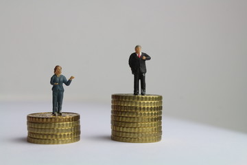 kleine Figuren auf unterschiedlich hohen Münzstapeln stehen für die ungleiche Bezahlung von...