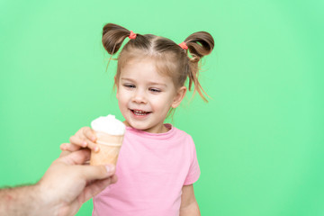 little girl 4 years old in a pink T-shirt on a green background holds out his hand to ice cream with delight, the child is happy