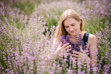 Beautiful girl in dress in purple lavender field. Beautiful woman walk on the lavender field. Girl collect lavender. Enjoy the floral glade, summer nature. Natural cosmetics and eco makeup concept.