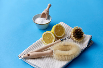natural cleaning stuff, sustainability and eco living concept - different brushes, washing soda powder with wooden scoop in bowl on blue background