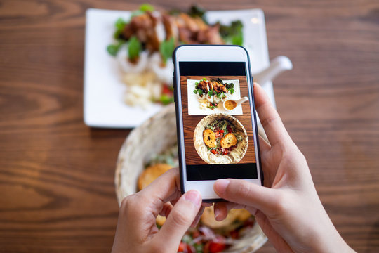 The hand of a woman using a mobile phone to take pictures of food on the table to review and upload to social networks