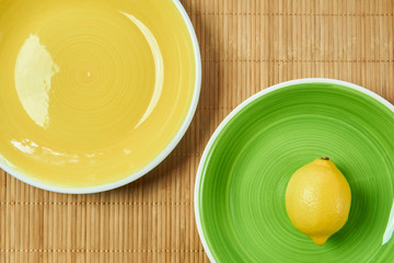 lemon on a green plate next to a yellow empty plate on a cane tablecloth