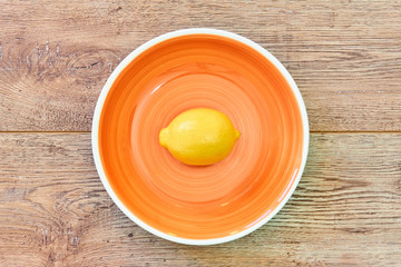 yellow lemon on a orange plate on a wooden tabletop