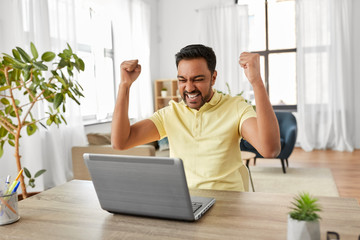 technology, remote job and lifestyle concept - happy indian man with laptop computer celebrating...