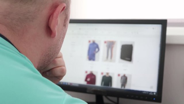 Shopping through a computer. A man looking and chooses wear in a clothing store to buy on the site. Browse a clothing to buy through a computer. Screen is blurred. Close Up.