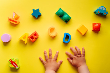 Child is playing with colorful constructor blocks. Kid's hands with bricks toy on yellow background. Educational toy, flat lay, top view.