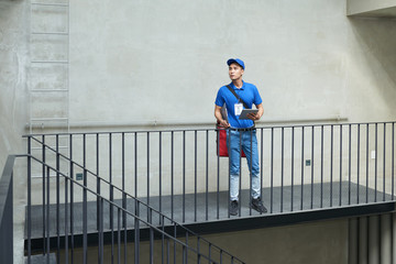 Lost delivery man with tablet computer in hands looking for apartment of customer