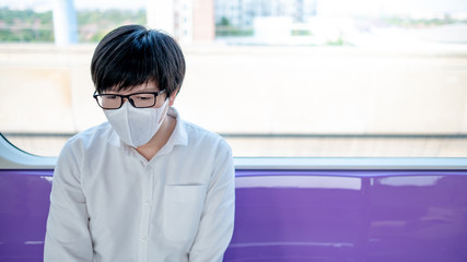 Asian man wearing surgical face mask sitting on skytrain or urban train. Coronavirus (COVID-19) outbreak prevention in public transportation. Social distancing for pandemic protection