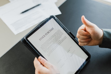 Man reading stock purchase agreement on tablet and showing thumbs up.