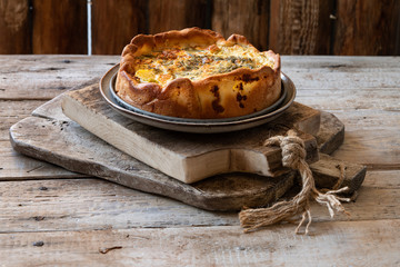 Homemade tasty open faced pie or quiche lorraine on light wooden table background.  traditional french pie with potatoes, gherkins, eggs, cheese, aromatic herbs.French cuisine, scandinavian style