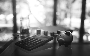 Black and white image of a calculator , piggy bank , coins stack and a glass money jar on the table...
