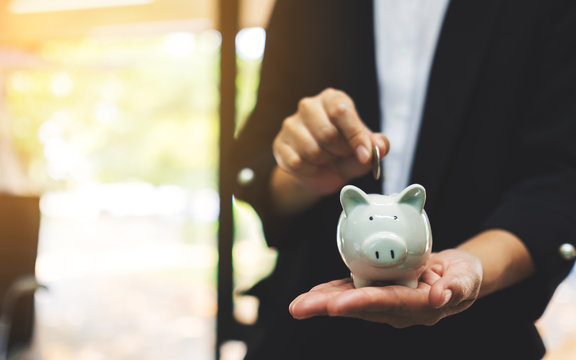 Closeup image of a businesswoman holding and putting coin into piggy bank for saving money and financial concept