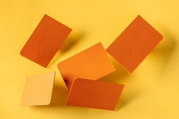 Thick orange business cards with a rounded corner, floating on a yellow paper background, a mockup...