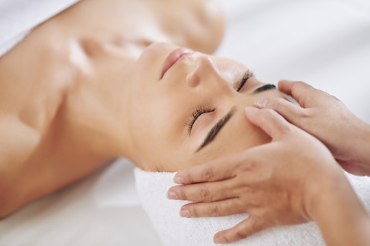 Close-up image of relaxed young woman getting rejuvenating face massage in beauty salon
