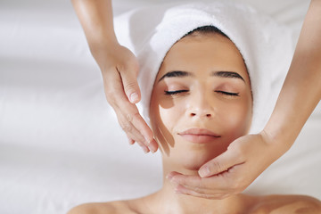 Smiling young woman getting anti-aging face massage in spa salon , view from above