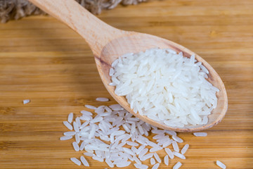 Uncooked basmati rice in wooden spoon on wooden surface closeup