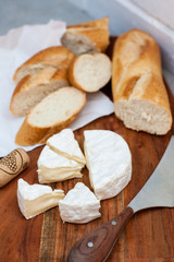 Two glasses of white wine, camemebert, cheese knife and baguette on wooden board.