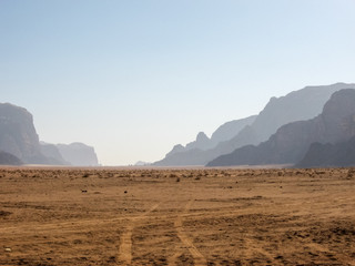 Fototapeta na wymiar Early morning in the Arabian desert. The tracks from the car's tires go in the direction of the silhouettes of mountains on the horizon.