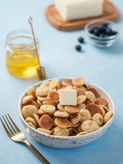 Trendy food - pancake cereal. Heap of mini cereal pancakes in boul on blue background. Copy space for text or design. Vertical.