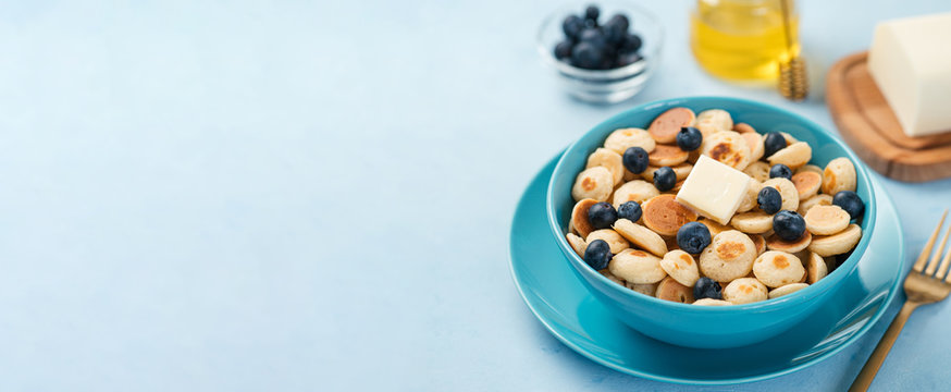 Trendy food - pancake cereal. Heap of mini cereal pancakes in boul on blue background. Copy space for text or design. Long horizontal banner