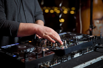 Dj mixes the track in the nightclub at party. Headphones in foreground and DJ hands in motion . Club party dj plays live set on stage in nightclub.