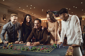 Happy people are betting in gambling at roulette poker in a casino - obrazy, fototapety, plakaty
