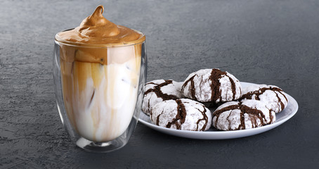 Double walled glass with dalgona coffee and chocolate chip cookie with cracks on a gray background.