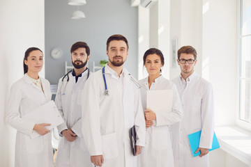 Fototapeta premium A group of confident practicing doctors in white coats are smiling against the backdrop of the clinic.