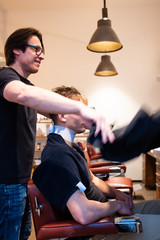 Barber swings his cape over young man in his barbershop