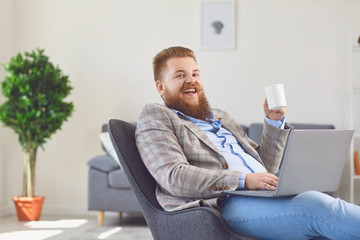 Work online at home office. Funny fat man works using a laptop in the apartment room.