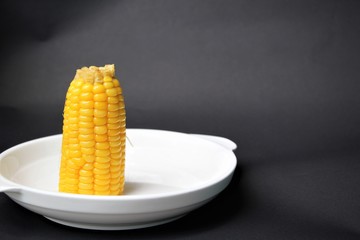 Corn on a white plate, a black background, Corn is a valuable plant that is a staple of Westerners,...