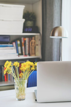 on the desktop is a laptop and next to dandelions in a vase