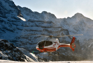 A red and white helicopter landing in the mountains