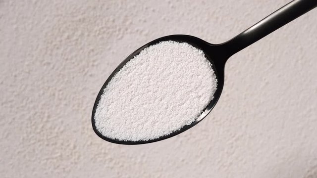 collagen powder in black spoon and collagen powder background rotating. Natural beauty and health supplement top view
