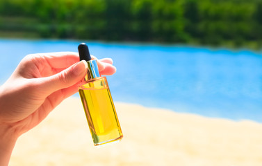 Unbranded glass container with dispenser on on the background of the beach and the sea. Transparent bottle with oil Product advertisement. Mockup style design. Cosmetology and beauty concept