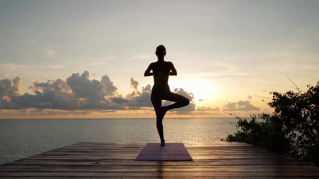 Doing yoga at sunrise, the girl practices the yoga tree pose, the harmony of the body with nature.
