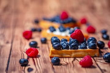 Sweet Homemade waffles with fresh raspberries, blueberries and cream on pink background