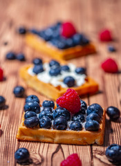 Sweet Homemade waffles with fresh raspberries, blueberries and cream on pink background