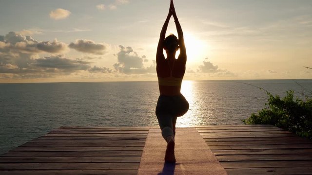 Silhouette of woman practices yoga and doing stretching at sunrise