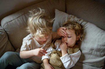 Two small sick children brother and sister at home lying in bed.