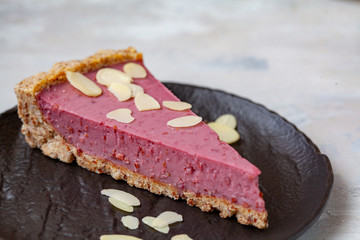 Slice of raw vegan berry cake with nuts on black saucer. Raw vegan dessert concept.