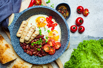 Fried eggs, sausages and beans - breakfast in pan, top view. Homemade breakfast concept.