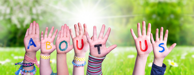 Children Hands Building Colorful English Word About Us. Sunny Green Grass Meadow As Background